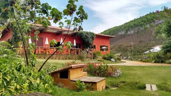 Chalé vermelho colonial com varanda e jardim florido na serra