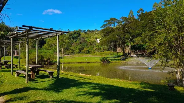 Lago sereno com pérgola de madeira, chafariz e montanhas ao fundo